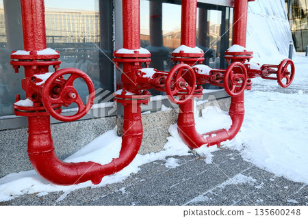 Red industrial gas pipes with valves covered in snow outdoors 135600248