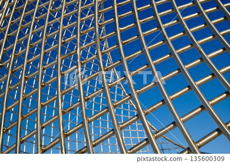 Modern metal mesh architecture detail with curved structure and blue sky Modern metal mesh architecture detail with curved structure and blue sky 135600309