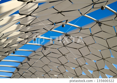 Futuristic architectural canopy roof with geometric panels, modern public space design, abstract structure against blue sky 135600322