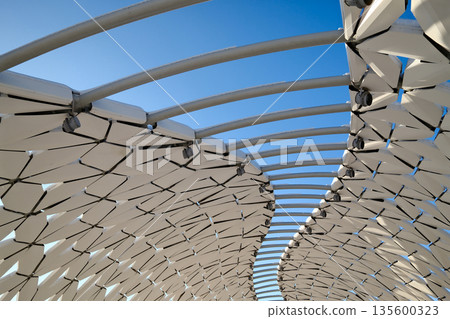 Futuristic architectural canopy roof with geometric panels, modern public space design, abstract structure against blue sky 135600323