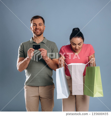 Black colored credit card, with shopping bags. Man and woman are in the studio Black colored credit card, with shopping bags. Man and woman are in the studio 135600435