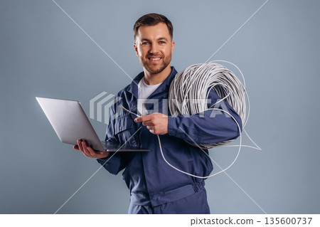 Laptop and internet cables, worker. Handsome man is against background Laptop and internet cables, worker. Handsome man is against background 135600737