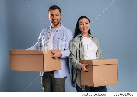 Against blue wall, with boxes, moving. Man and woman are in the studio Against blue wall, with boxes, moving. Man and woman are in the studio 135601003