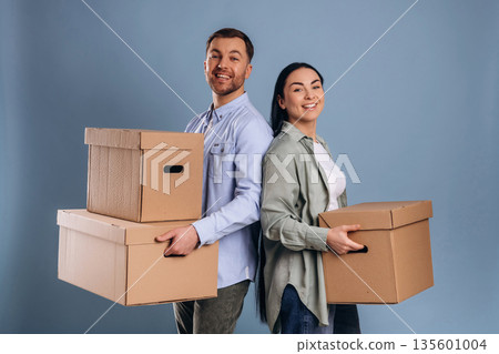 Against blue wall, with boxes, moving. Man and woman are in the studio Against blue wall, with boxes, moving. Man and woman are in the studio 135601004