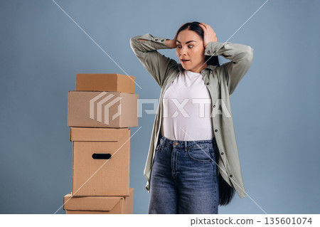 Shocked, looking at many boxes, moving. Beautiful woman is against background 135601074