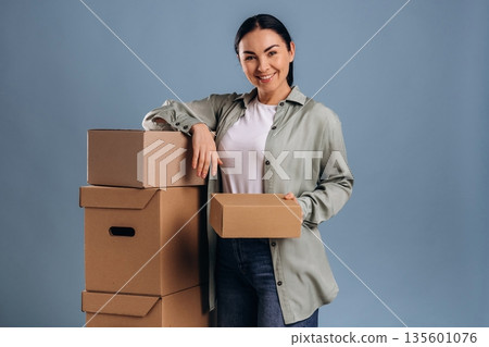Standing with the boxes, moving. Beautiful woman is against background 135601076