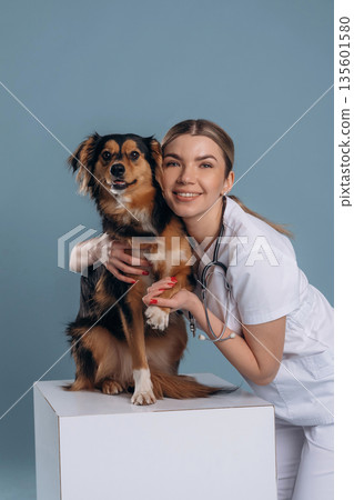 Embracing the animal, smiling. Woman veterinarian is with mixed-breed dog 135601580