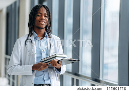 Learning material, books in hands. Young male black doctor is in the corridor 135601758
