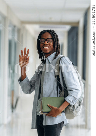 Bye hand gesture, smiling. Student with backpack is in the corridor Bye hand gesture, smiling. Student with backpack is in the corridor 135601785