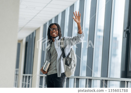 Bye hand gesture, smiling. Student with backpack is in the corridor Bye hand gesture, smiling. Student with backpack is in the corridor 135601788