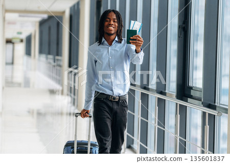 Passport and tickets in hand. Male tourist is in the airport corridor 135601837