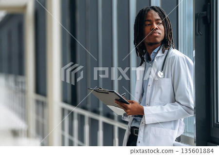 Side view. Young male black doctor is in the corridor Side view. Young male black doctor is in the corridor 135601884