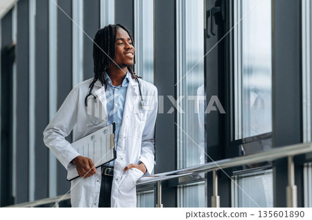 Leaning on the railings near windows. Young male black doctor is in the corridor 135601890