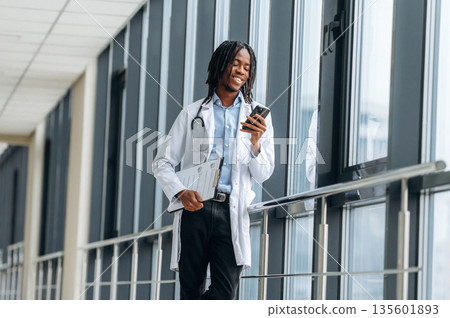 Joyful, positive facial expression. Young male black doctor is in the corridor Joyful, positive facial expression. Young male black doctor is in the corridor 135601893