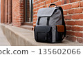 Stylish grey backpack on urban brick wall in city environment 135602066