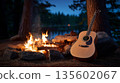 Acoustic guitar by campfire at dusk in forest setting 135602067