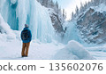 Young male adventurer exploring majestic frozen waterfall in snowy mountain landscape 135602076