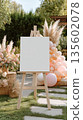 Elegant outdoor wedding decor with blank canvas on easel surrounded by flowers and balloons 135602078
