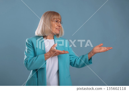 Showing to the side. Senior woman is against background Showing to the side. Senior woman is against background 135602118