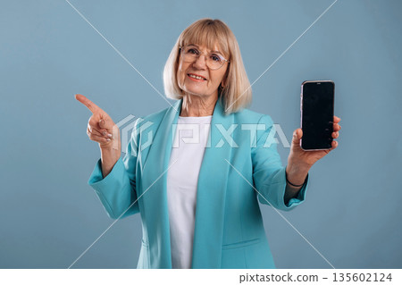 Smartphone with copy space, showing to the side. Senior woman is against background Smartphone with copy space, showing to the side. Senior woman is against background 135602124