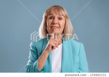 Be silent, finger before the lips. Senior woman is against background 135602131