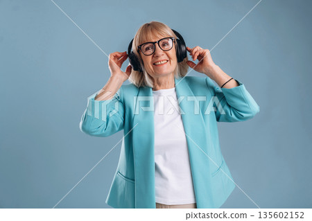 Listening to music, enjoying. Senior woman is against background Listening to music, enjoying. Senior woman is against background 135602152
