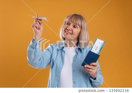 Tickets in hands, ready for vacation. Senior woman is against background Tickets in hands, ready for vacation. Senior woman is against background 135602216