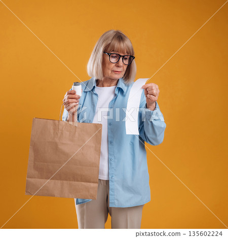 Shopping concept, too expensive, with check. Senior woman is against background Shopping concept, too expensive, with check. Senior woman is against background 135602224