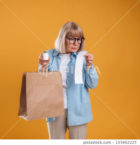 Shopping concept, too expensive, with check. Senior woman is against background Shopping concept, too expensive, with check. Senior woman is against background 135602225
