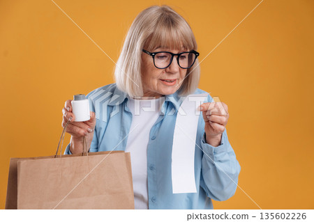 Shopping concept, too expensive, with check. Senior woman is against background Shopping concept, too expensive, with check. Senior woman is against background 135602226