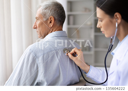 Female doctor examining senior male patients back with stethoscope in medical office 135604222
