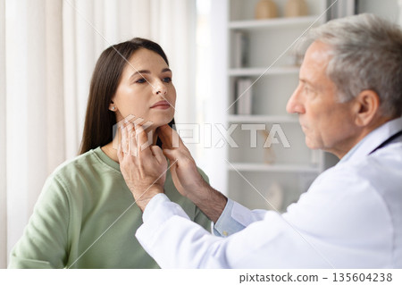 Male doctor palpating neck lymph nodes of female patient in clinic Male doctor palpating neck lymph nodes of female patient in clinic 135604238