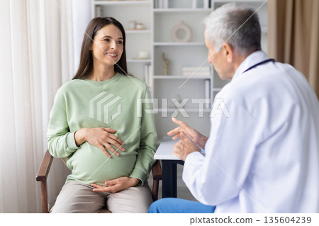 Pregnant woman consulting with senior male doctor during prenatal visit in clinic Pregnant woman consulting with senior male doctor during prenatal visit in clinic 135604239