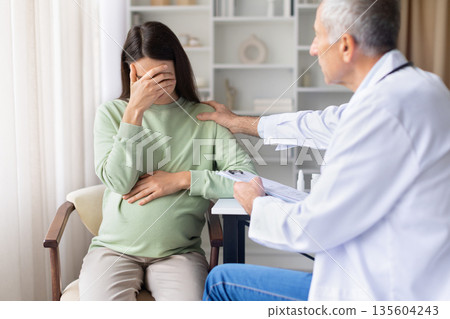 Emotional pregnant woman receiving support from senior male doctor during medical consultation Emotional pregnant woman receiving support from senior male doctor during medical consultation 135604243
