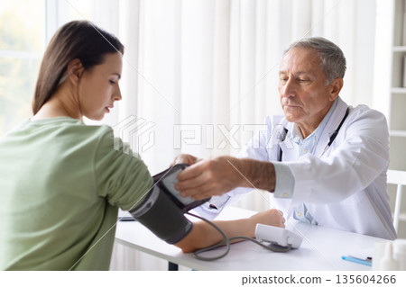 Male doctor measuring blood pressure of female patient using tonometer in clinic Male doctor measuring blood pressure of female patient using tonometer in clinic 135604266