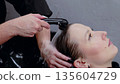 Hairdresser rinsing shampoo from client's hair with shower head in beauty salon, providing professional hair care service 135604729