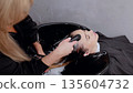 Skilled hairdresser giving a high quality hair wash to a young woman in a beauty salon using shampoo and a shower head 135604732