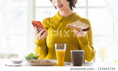 一名女子一邊吃飯一邊看著智慧型手機 一名女子一邊吃飯一邊看著智慧型手機 135604739