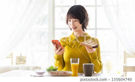 A woman eating while looking at her smartphone A woman eating while looking at her smartphone 135604740
