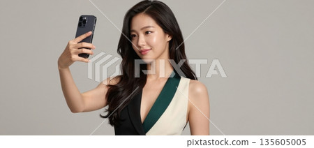 Confident stylish young woman taking a selfie with smartphone on a clean minimal studio background 135605005
