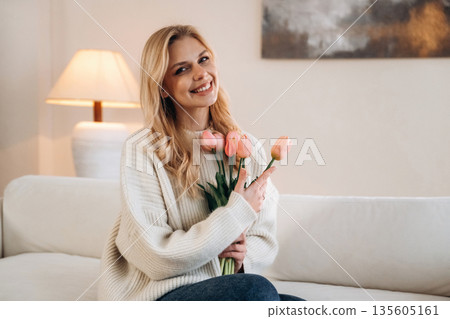 Happy facial expression. Beautiful young woman is at home with flowers Happy facial expression. Beautiful young woman is at home with flowers 135605161