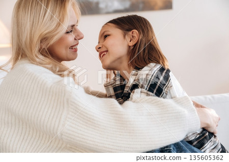 Closeness, sitting on the sofa. Mother and daughter are together in domestic room 135605362