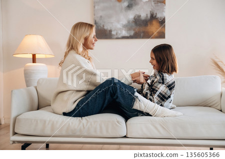 Cozy, sitting on the sofa, side view. Mother and daughter are together in domestic room Cozy, sitting on the sofa, side view. Mother and daughter are together in domestic room 135605366