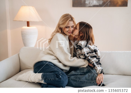 Cozy, sitting on the sofa, side view. Mother and daughter are together in domestic room Cozy, sitting on the sofa, side view. Mother and daughter are together in domestic room 135605372