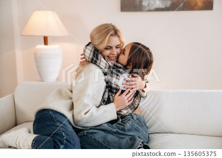 Cozy, sitting on the sofa, side view. Mother and daughter are together in domestic room Cozy, sitting on the sofa, side view. Mother and daughter are together in domestic room 135605375