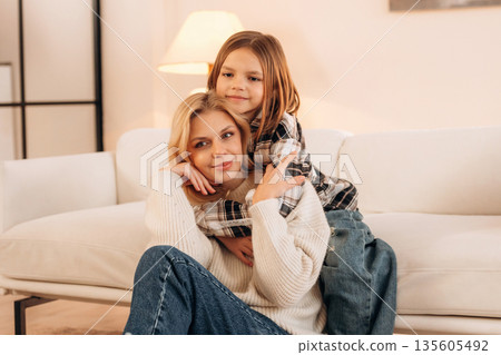 Adorable, lovely hugs. Mother and daughter are together in domestic room Adorable, lovely hugs. Mother and daughter are together in domestic room 135605492