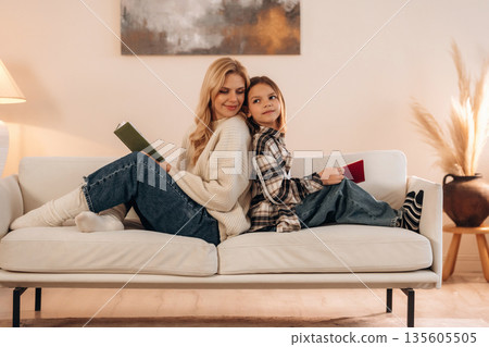 With books, reading time. Mother and daughter are together in domestic room With books, reading time. Mother and daughter are together in domestic room 135605505