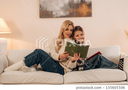 With books, reading time. Mother and daughter are together in domestic room With books, reading time. Mother and daughter are together in domestic room 135605506