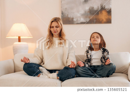 Lotus pose, meditation. Mother and daughter are together in domestic room 135605521