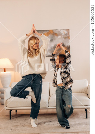 Standing on one leg, sport and yoga. Mother and daughter are together in domestic room Standing on one leg, sport and yoga. Mother and daughter are together in domestic room 135605525